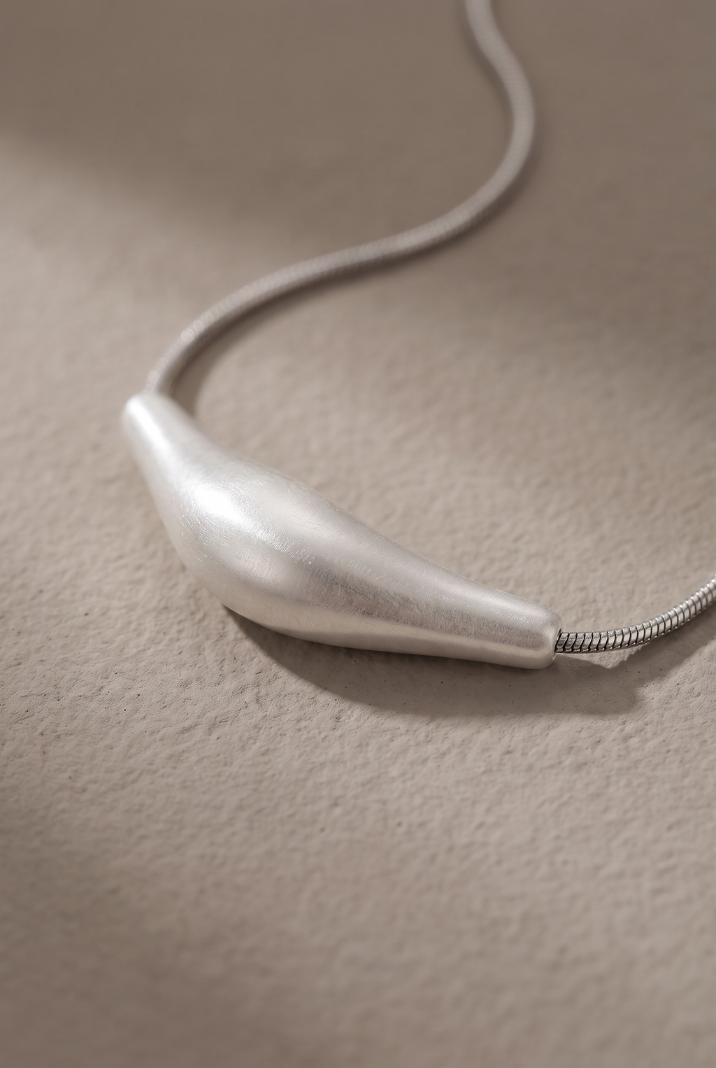 Close-up of the brushed bar pendant threaded on the snake chain